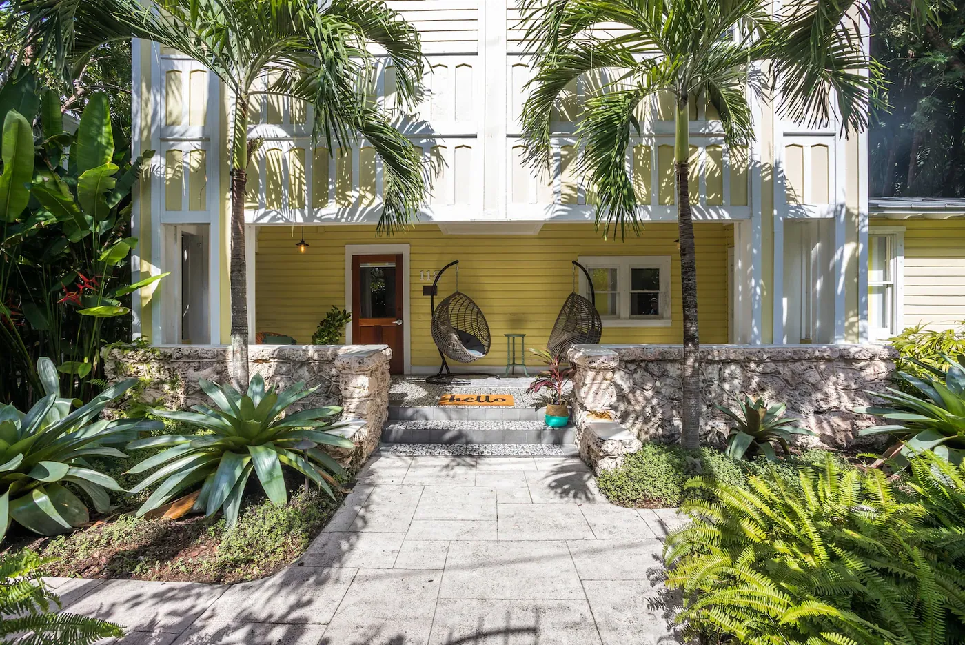 The yellow clapboard house behind a coral rock wall, bromeliads in the planting