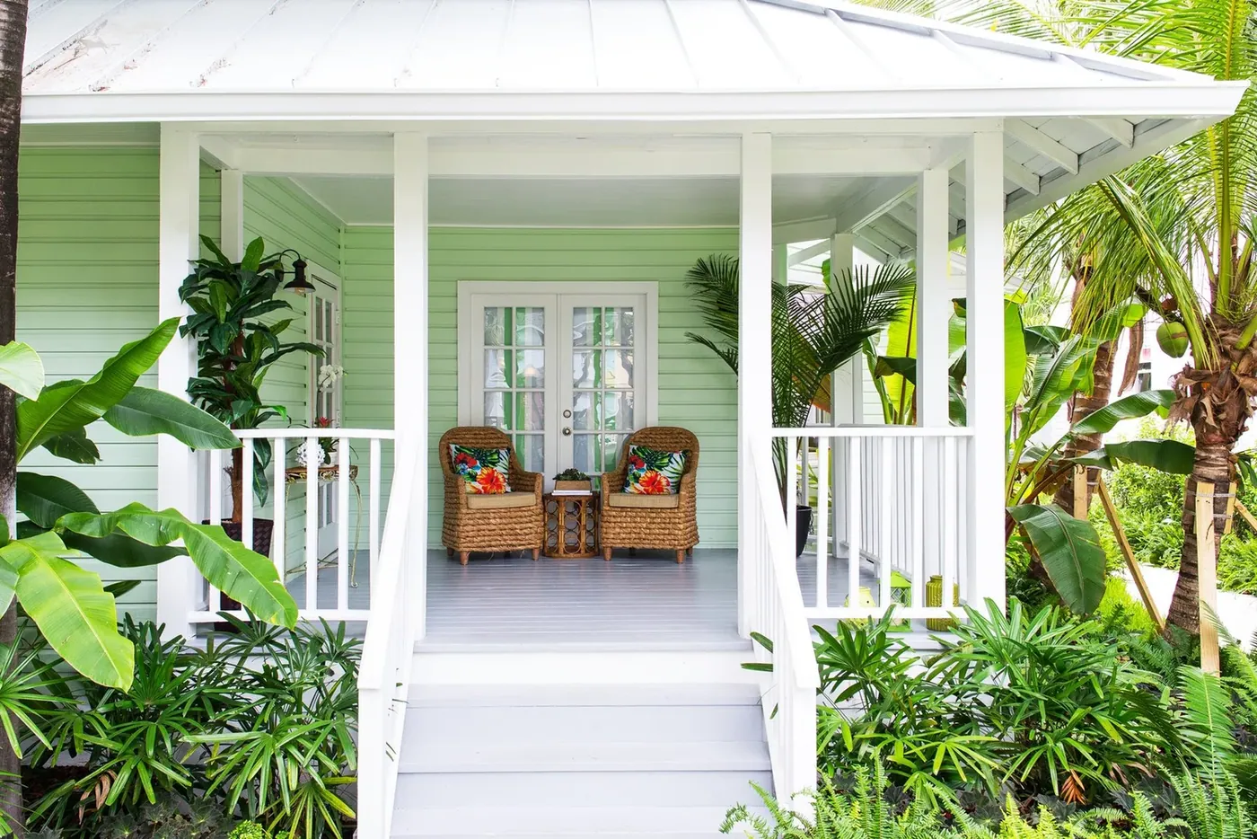 Rocking chairs on the shaded porch of a green cottage